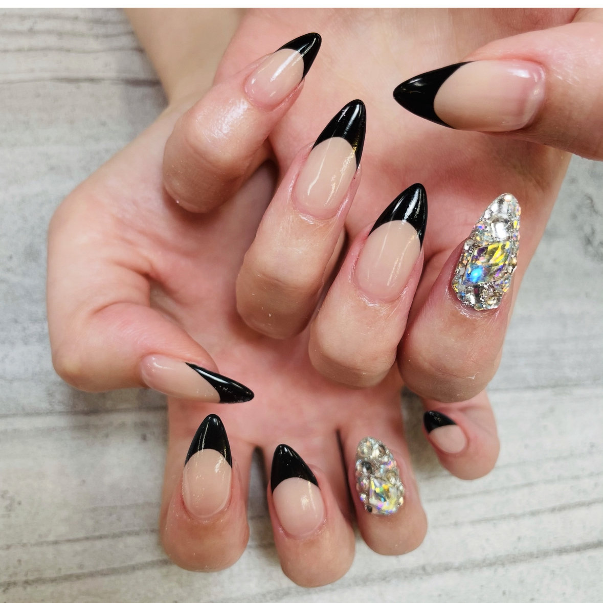 Nude almond nails with black french tips and crystal accent nails
