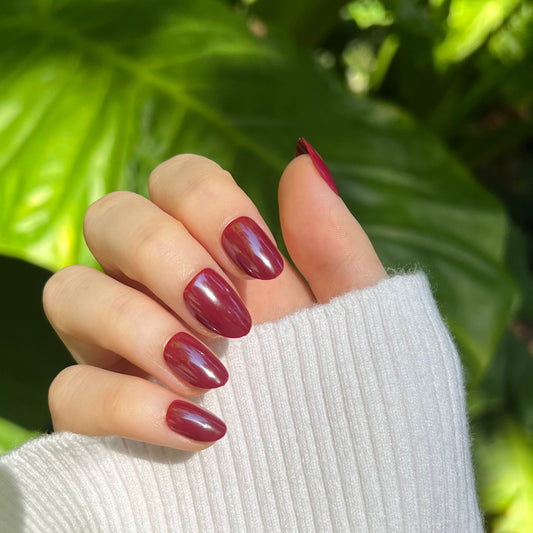 Glossy burgundy short almond nails on a hand in a white sweater cuff