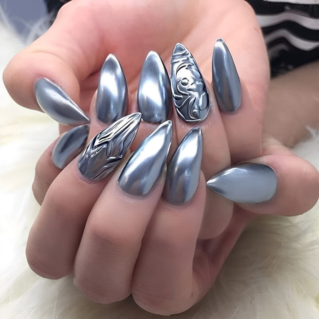 Long stiletto nails in pewter-silver chrome with two 3D embossed scrollwork accent nails; real photography.