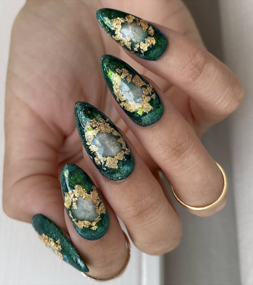 Stiletto nails in deep emerald green with gold foil flakes