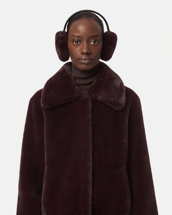 Woman wearing dark brown faux fur earmuffs and a dark brown faux fur coat with a turtleneck