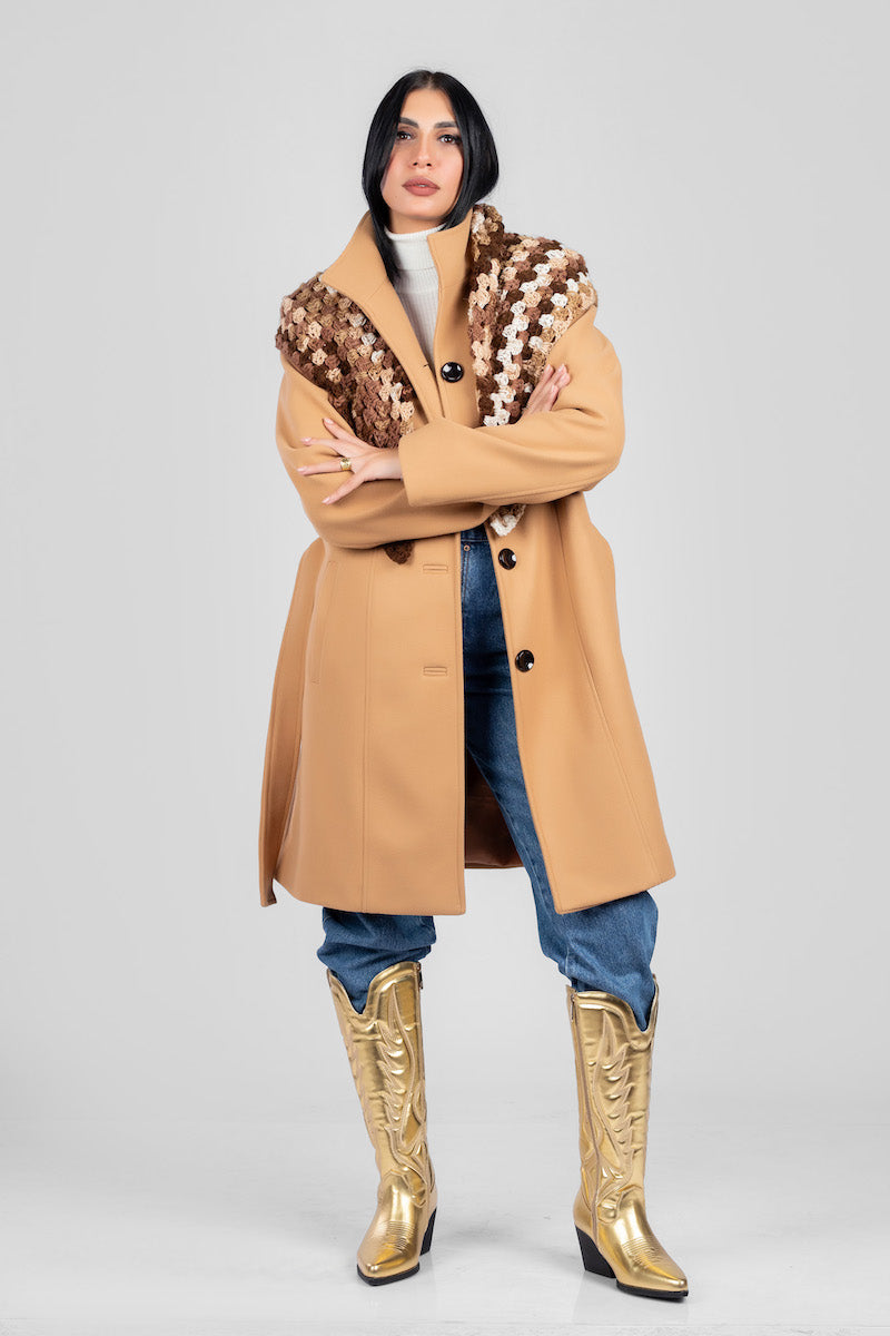 Woman in a camel coat and white turtleneck with metallic gold cowboy boots in a studio portrait