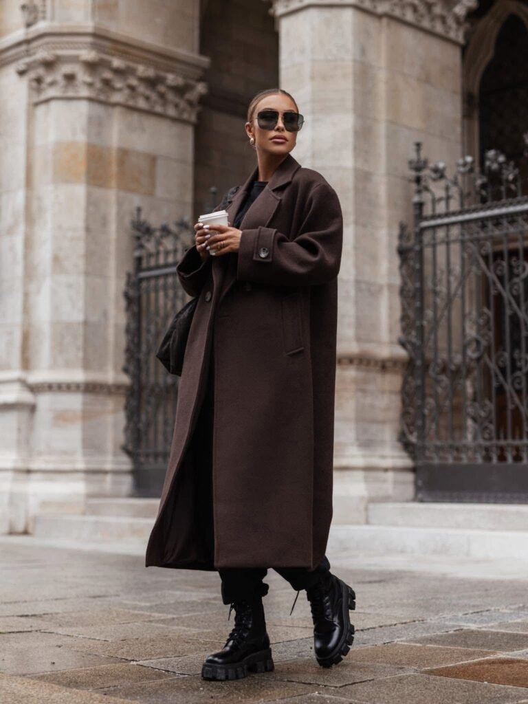 Woman in a chocolate brown long wool coat with black layers and chunky black combat boots