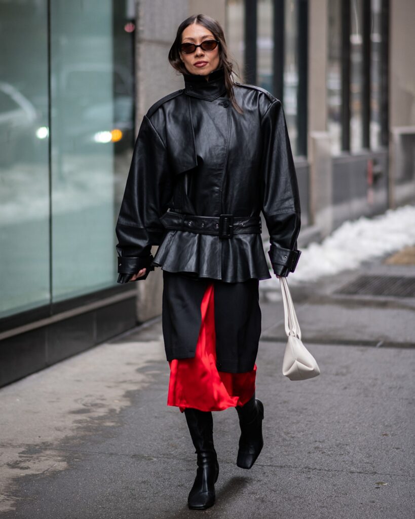 Woman wearing a belted black leather jacket over a red satin skirt with knee-high boots
