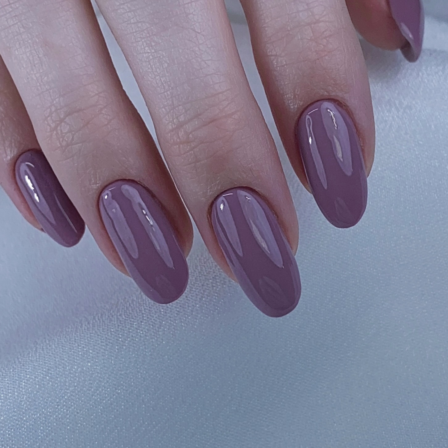 Medium oval nails in a muted dusty-mauve crème with a glossy finish; real photography.