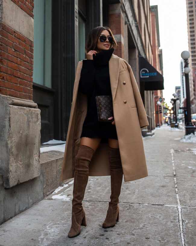 Woman in a camel coat over a black turtleneck sweater dress with brown suede over-the-knee boots