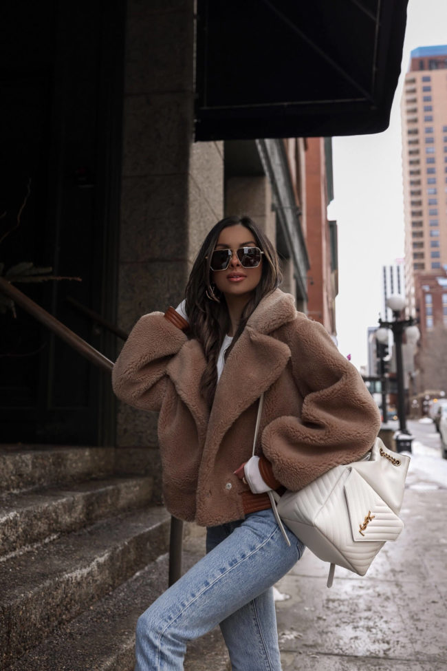 Woman wearing a tan teddy shearling jacket with a white top and light-wash jeans