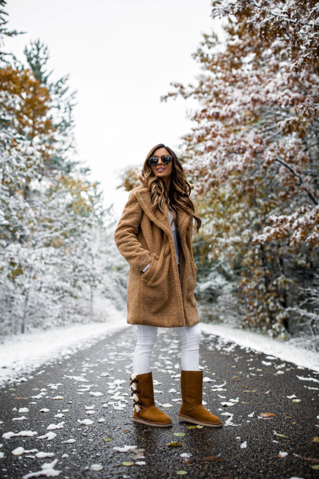 Woman in a brown teddy coat with white jeans and tan winter boots on a snowy path