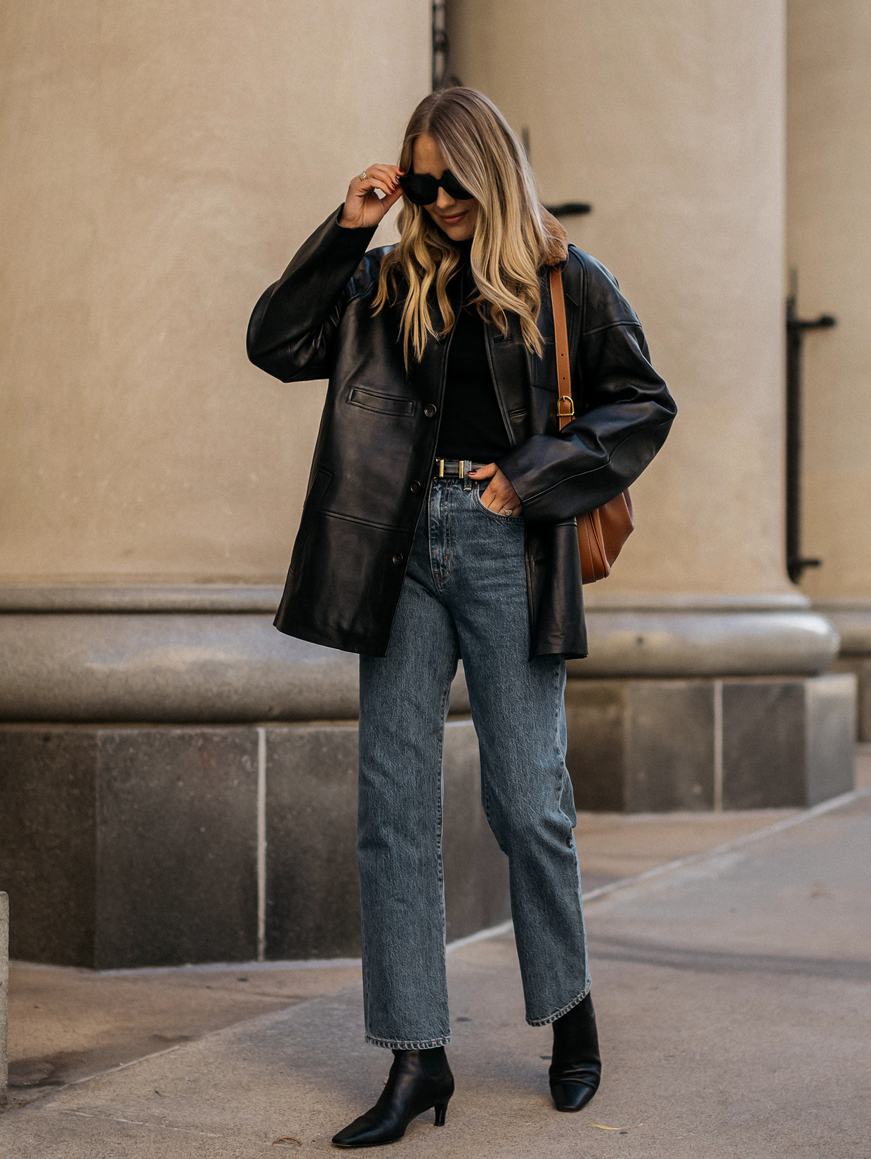 Woman in a black faux leather moto jacket, skinny jeans and ankle boots in a winter street-style look