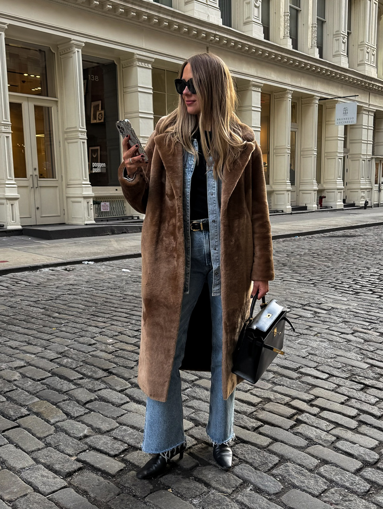 Woman in a long brown fuzzy coat over a chambray shirt and jeans with black ankle boots
