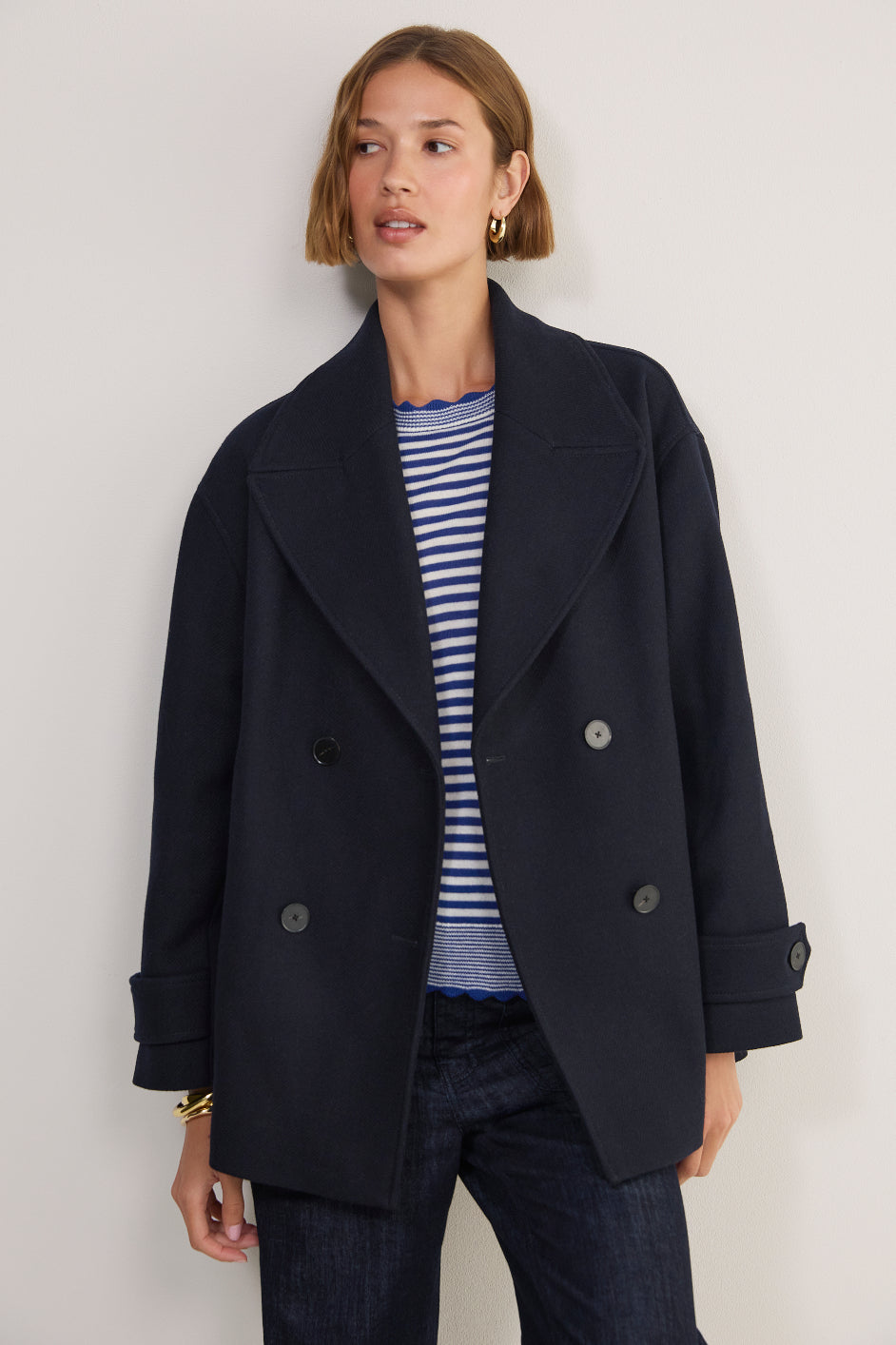 Woman in a navy double-breasted peacoat with a blue striped knit and dark jeans