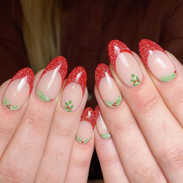 Almond nails with red glitter French tips and tiny hand-painted holly and berry cuticle art on a nude base.