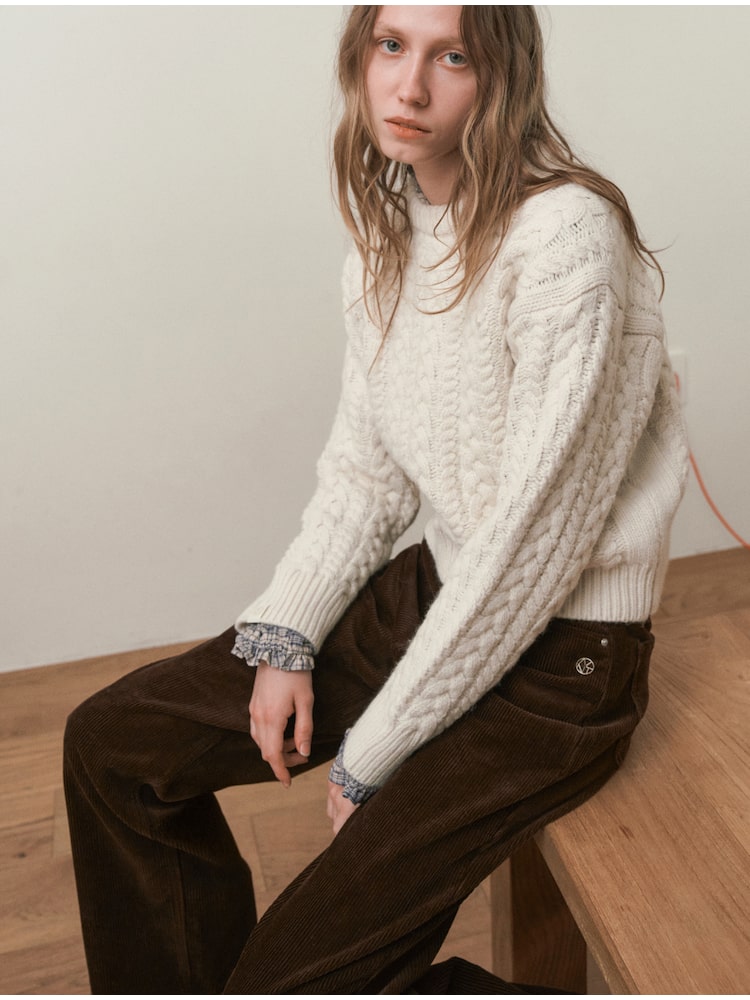 Woman seated wearing a cream cable-knit sweater and chocolate-brown corduroy trousers