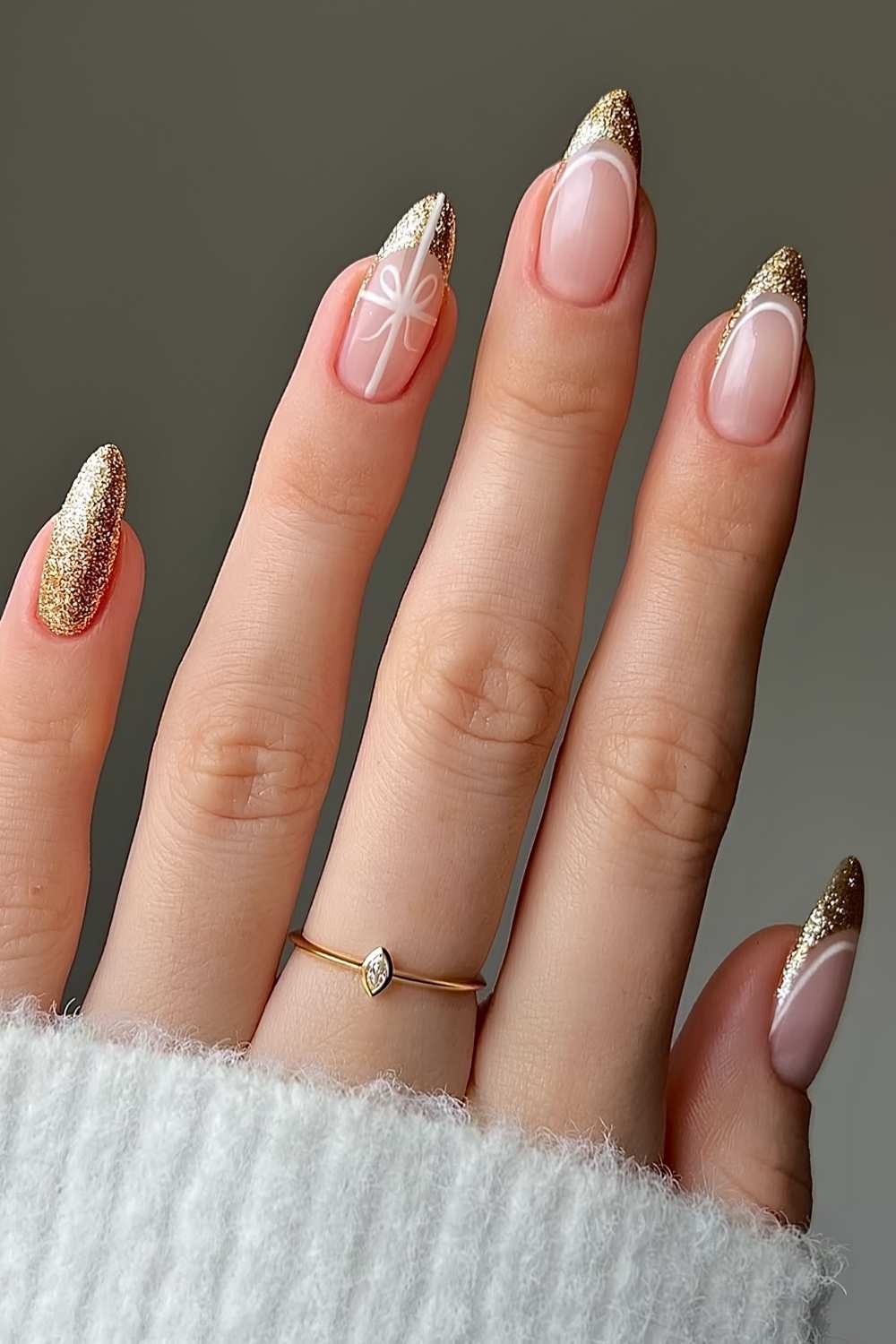 Long almond nails with gold glitter French tips and a white hand-painted bow on one accent nail