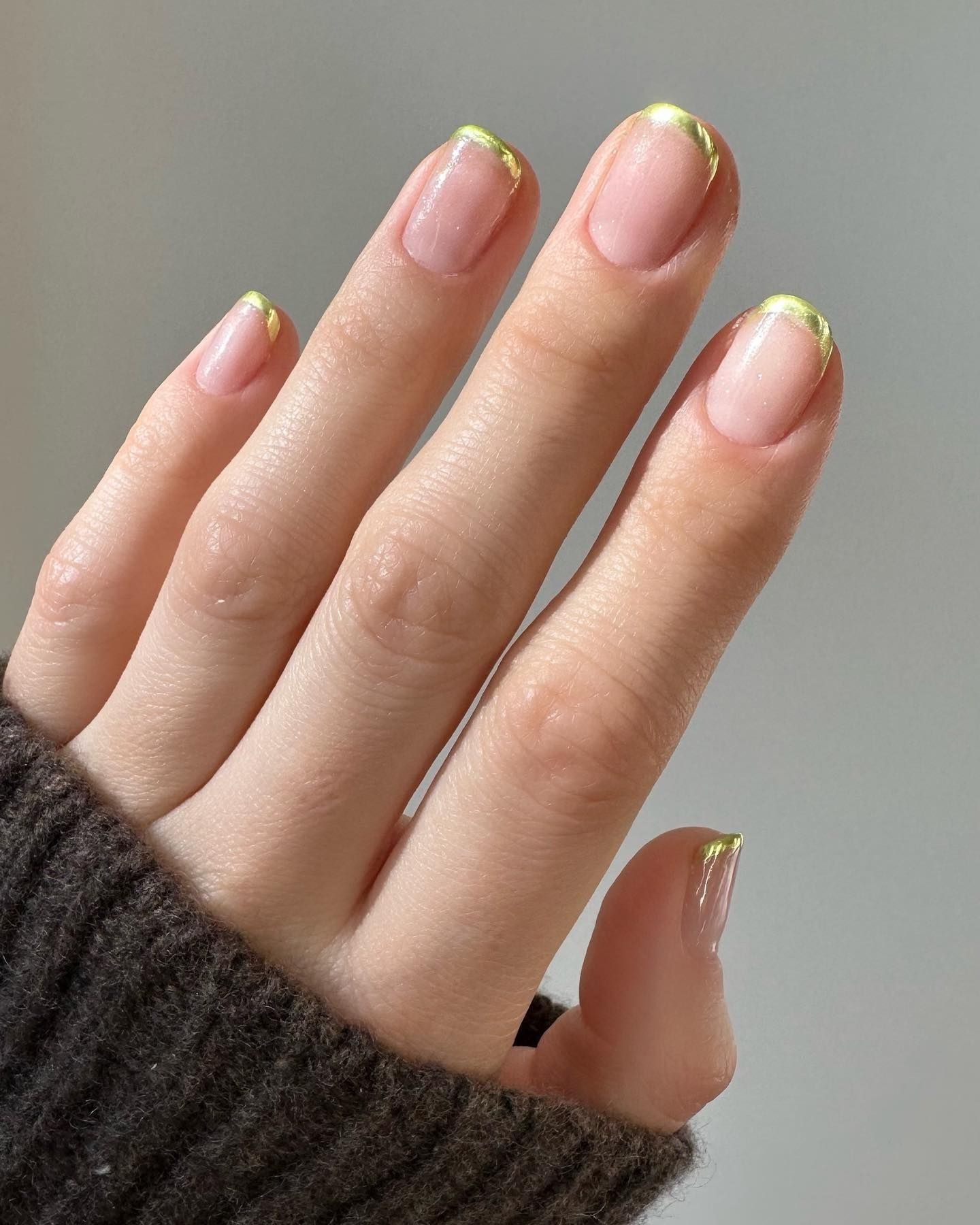 Short oval nails with gold micro-French tips on a sheer pink base