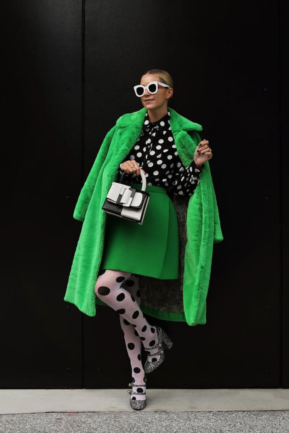 Woman wearing a bright green faux-fur coat with a polka-dot blouse, green skirt and glitter heels