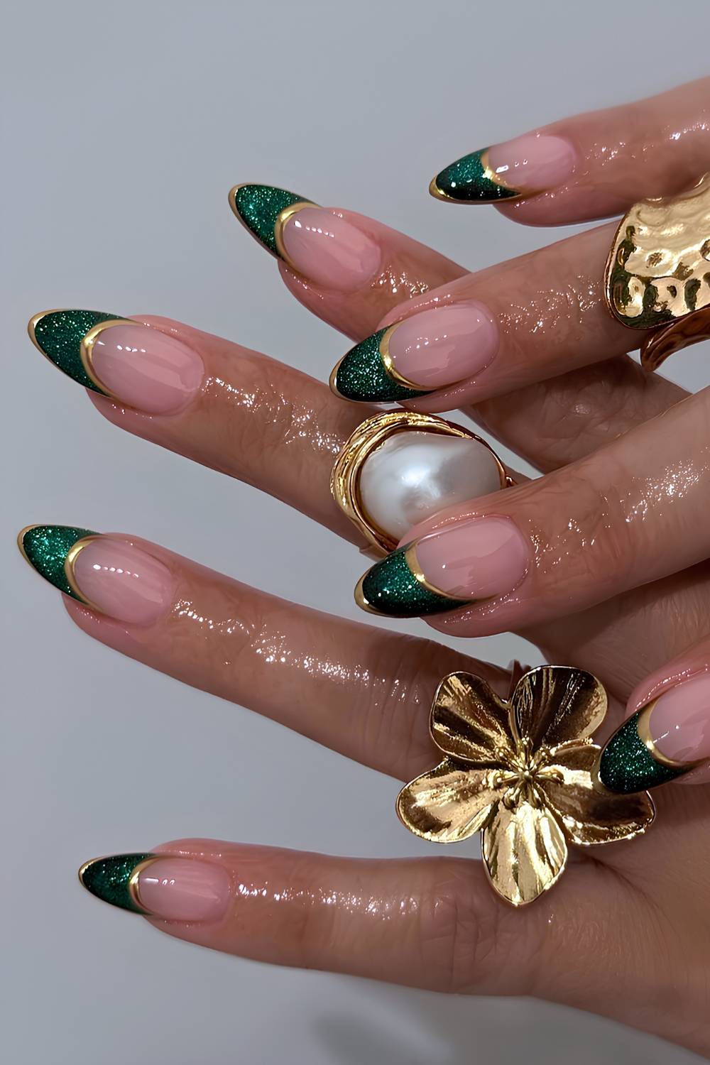 Almond nails with a nude base and emerald green glitter French tips outlined in thin gold chrome