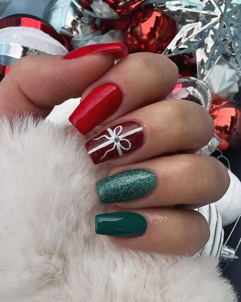 Glossy red nails with a white gift-wrap ribbon bow accent, green glitter and solid green nails