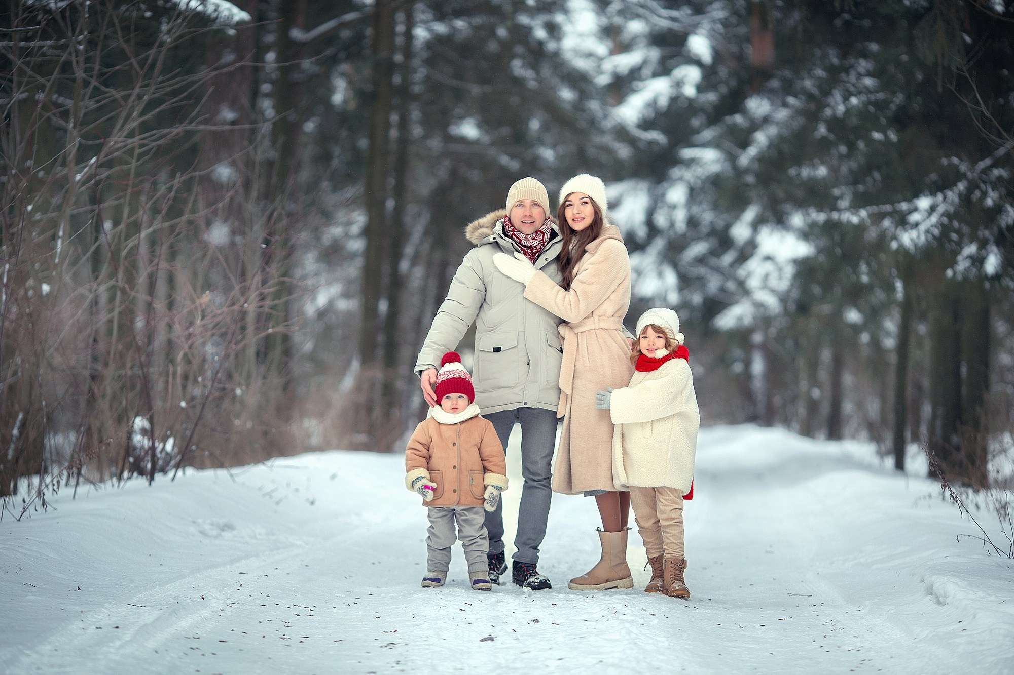Family in matching cream coats in the snow during a winter photoshoot