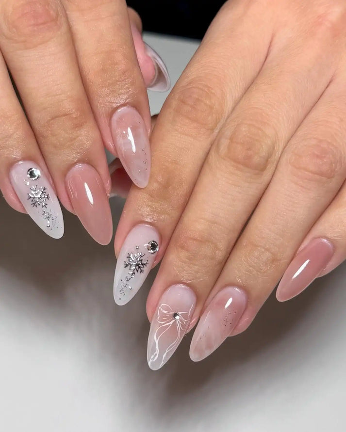 Nude almond nails with silver bow line art, white snowflakes and small gem accents