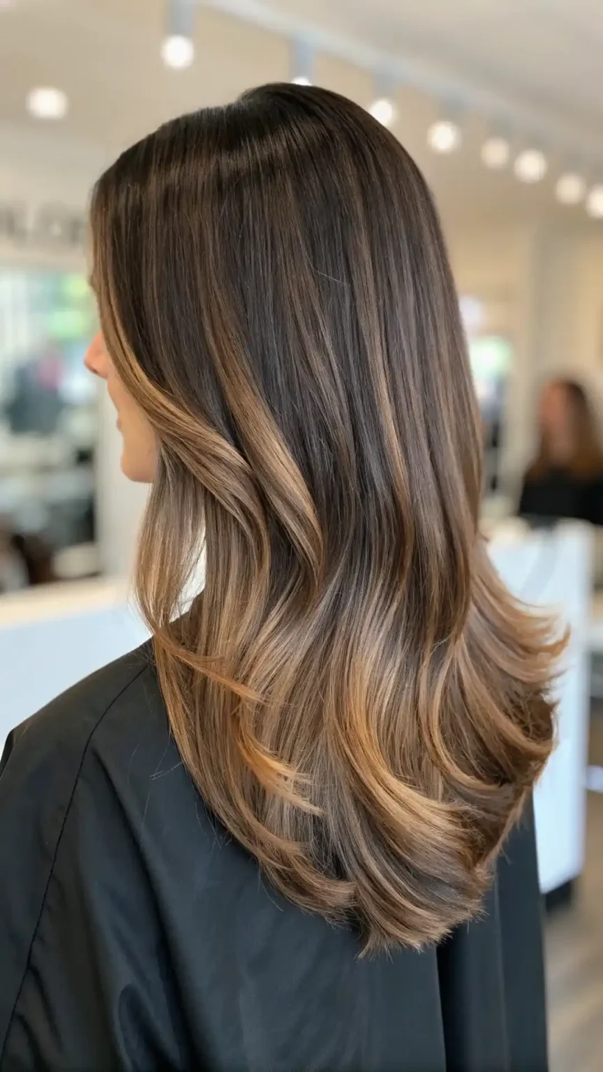 Side view of dark brown wavy hair with golden sunlit balayage highlights