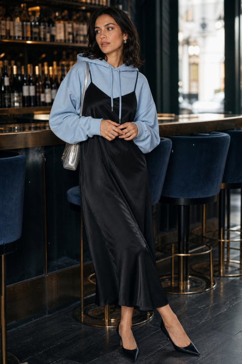Woman in light blue hoodie layered under black satin slip dress with pointed pumps