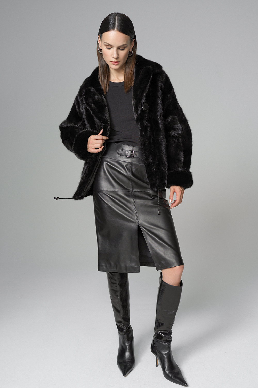 Model in black faux fur coat with black belted leather midi skirt and knee-high boots