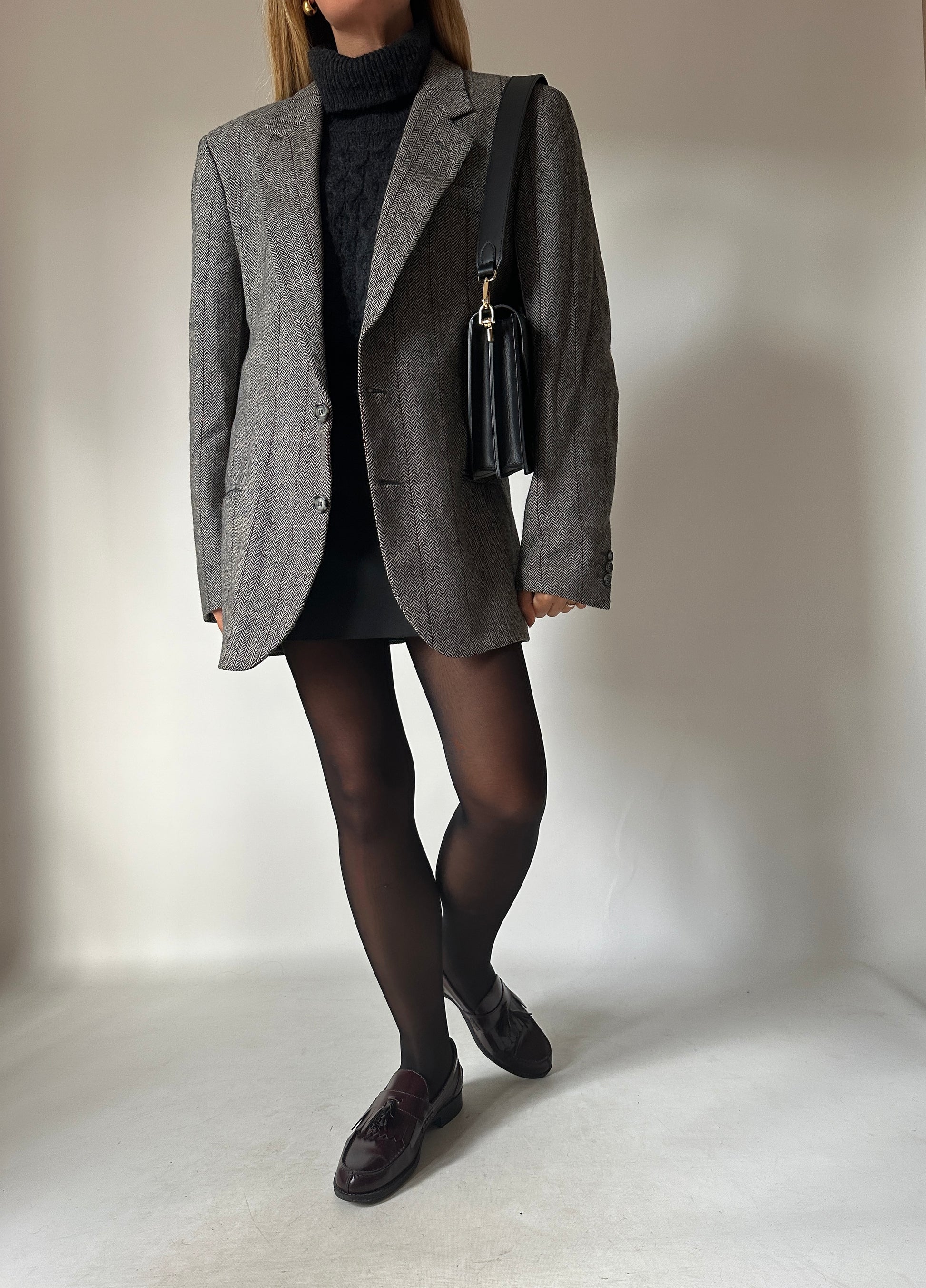 Woman in a grey herringbone blazer with a black turtleneck, mini skirt and loafers