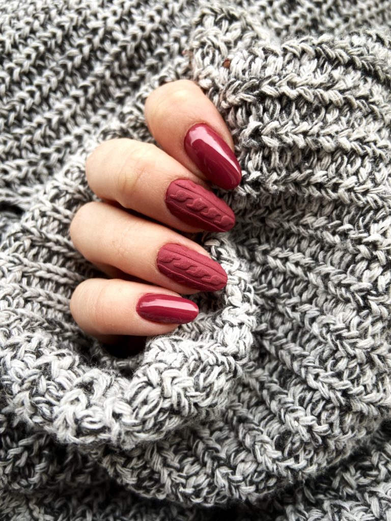Short almond nails in glossy wine-burgundy with a raised cable-knit sweater texture on alternating nails