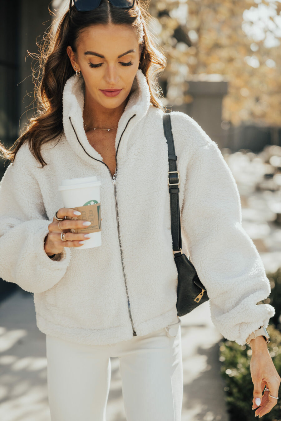 Woman in ivory sherpa zip jacket and white jeans holding a coffee