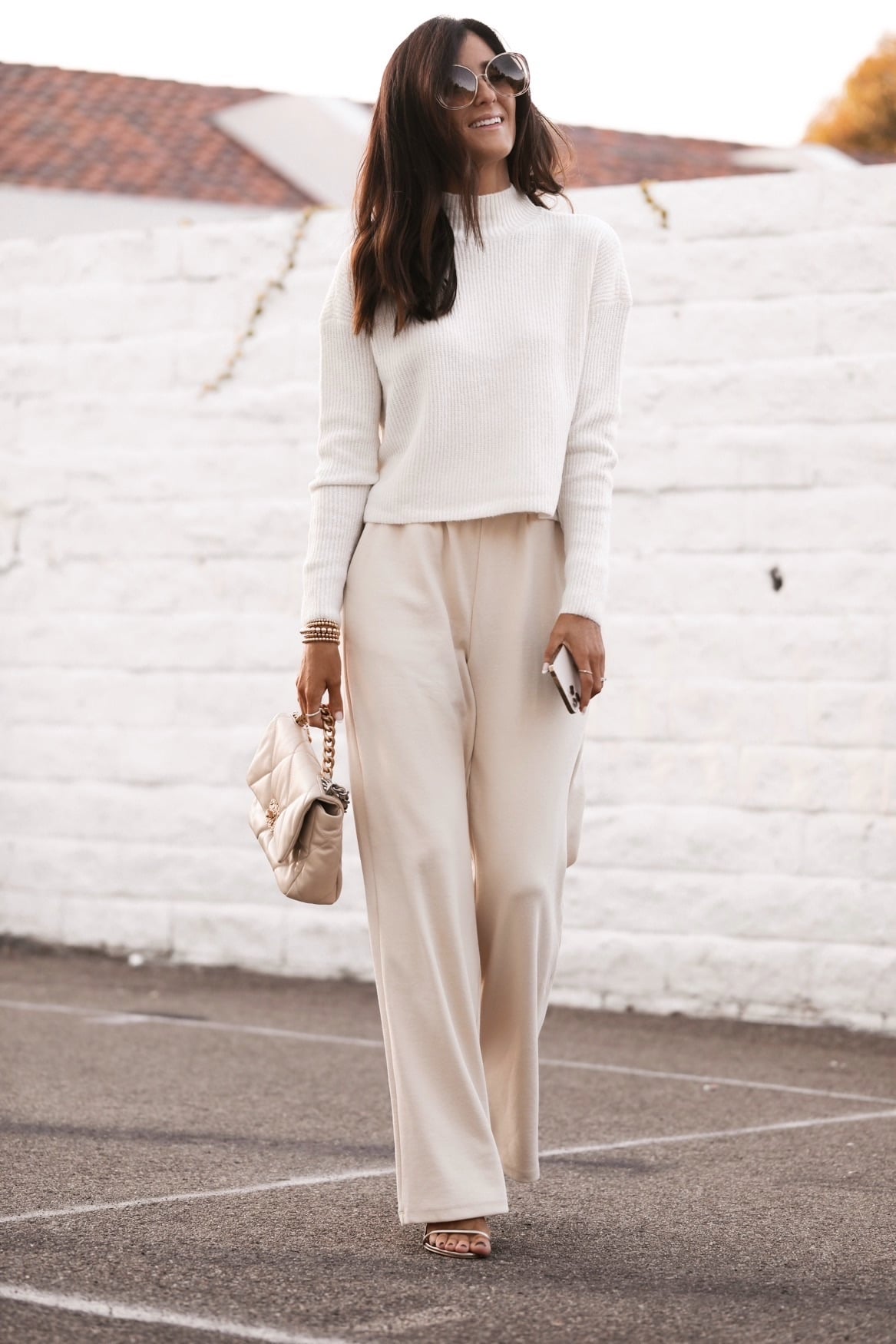 Woman wearing a white ribbed mock-neck sweater with cream wide-leg trousers and a quilted bag
