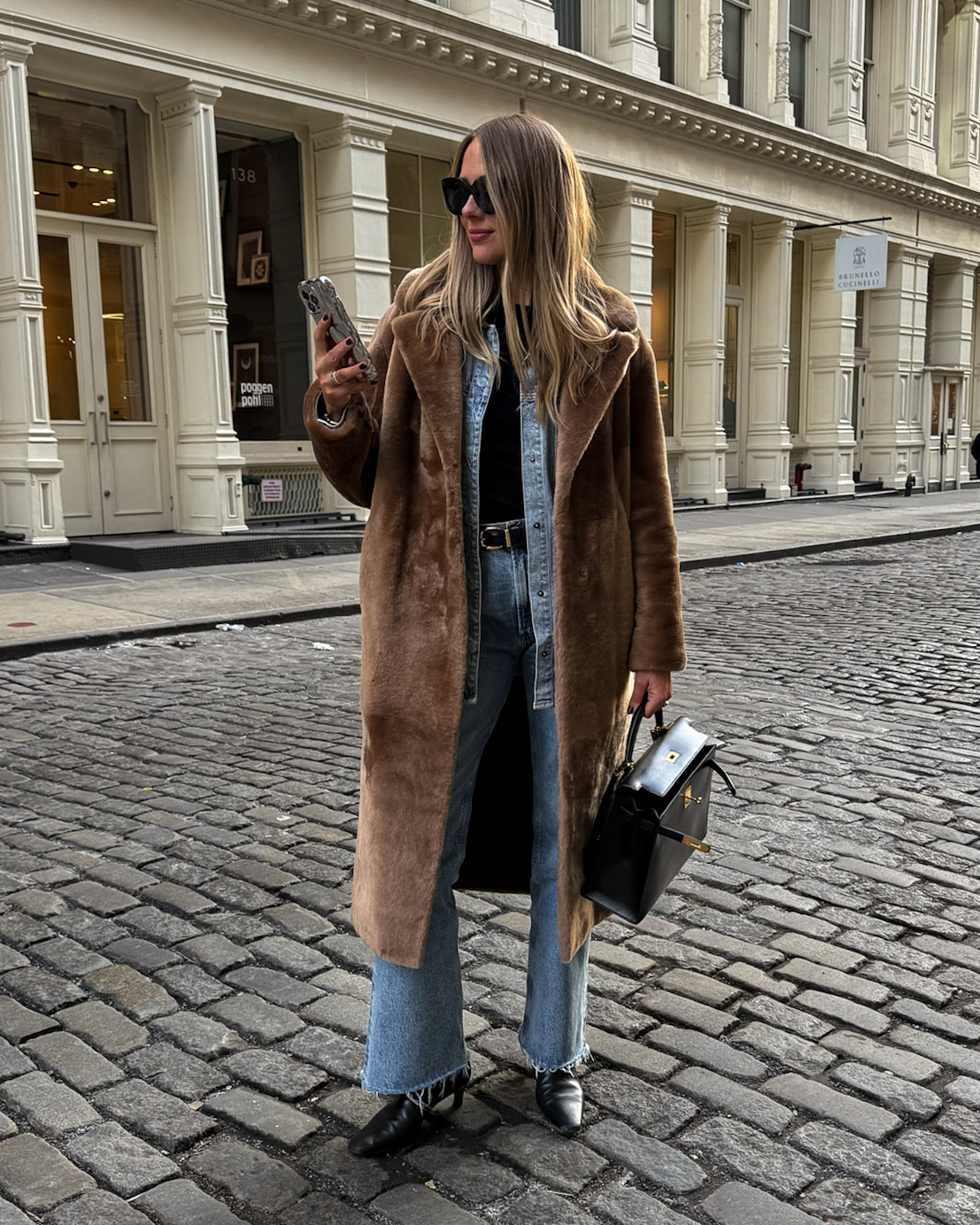 Woman wearing a brown faux-fur coat over a denim shirt and jeans with black boots