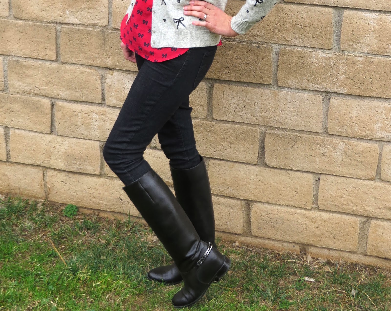 woman in bow-print blouse, cardigan, black skinny jeans and black tall boots