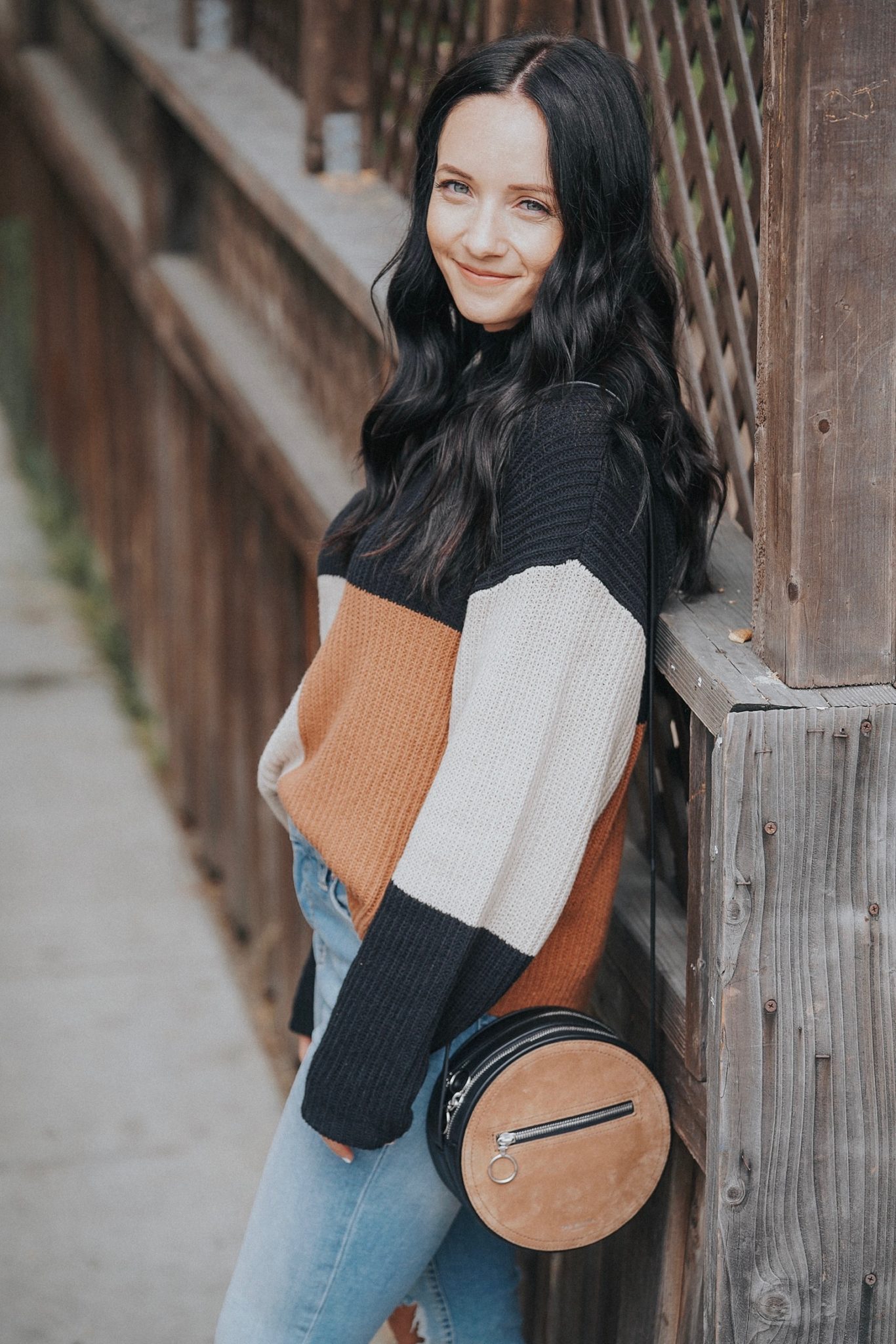 Woman wearing a black, camel and cream color-block sweater with light-wash jeans
