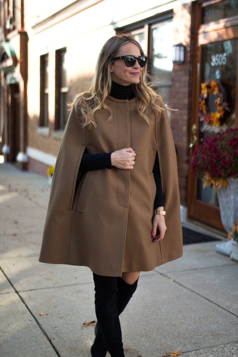 Camel cape coat over a black turtleneck with black over-the-knee boots