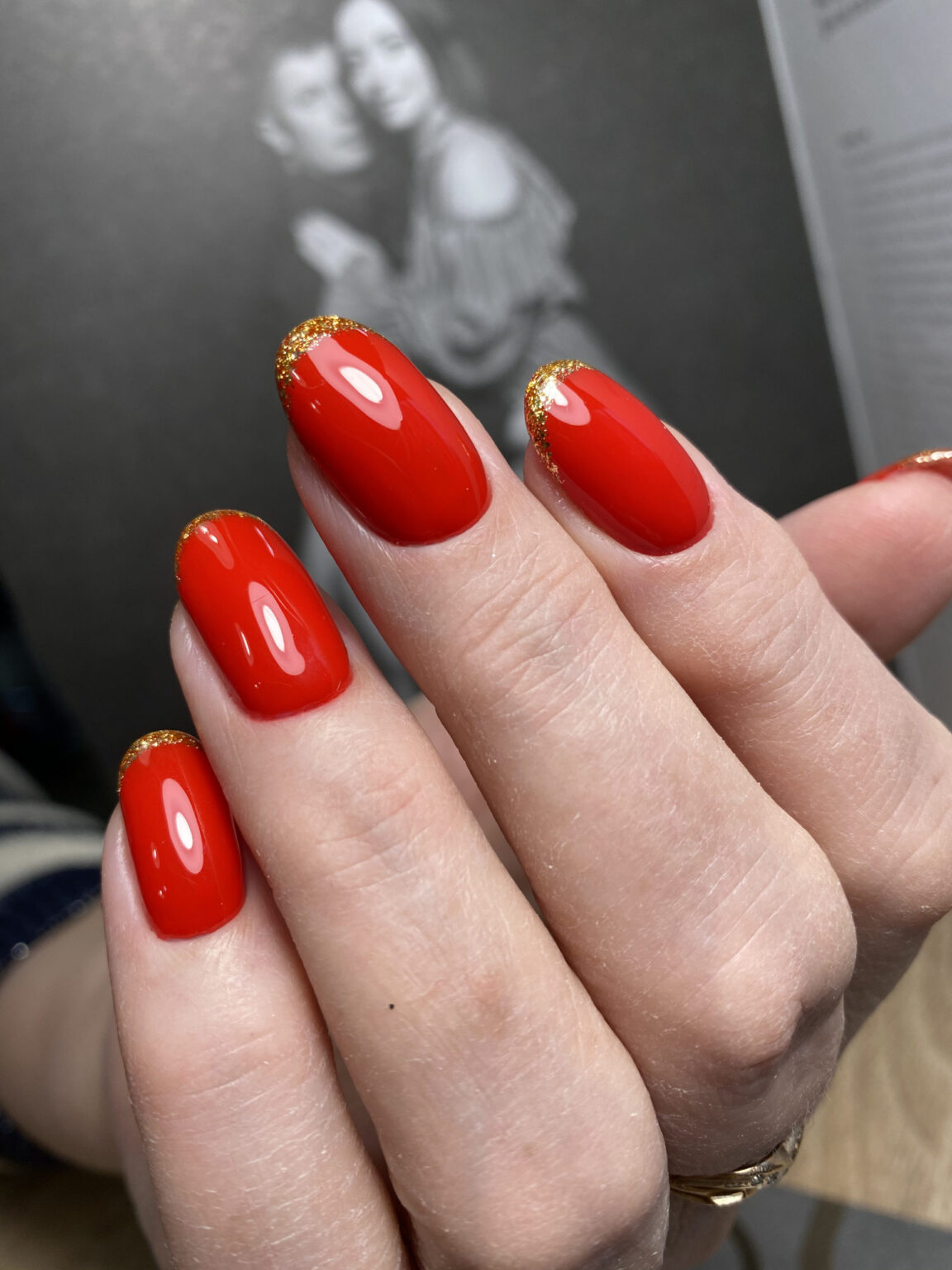 Oval bright red nails with gold glitter bands along the cuticles