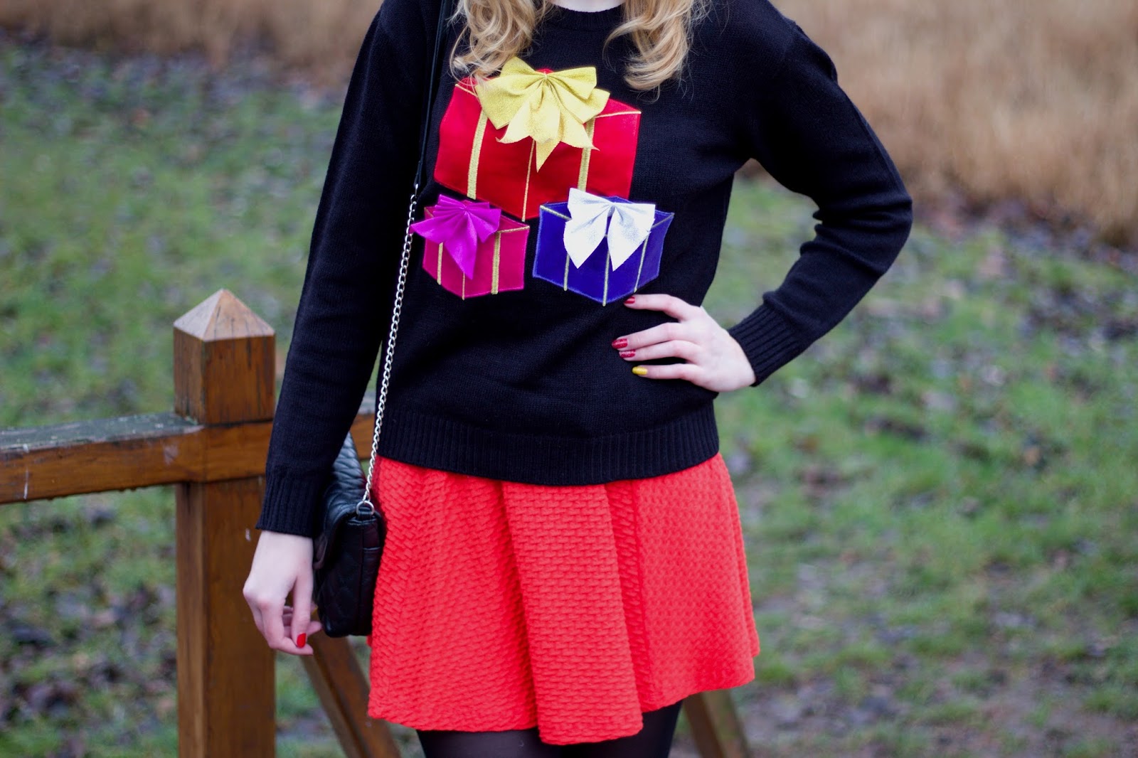 Woman wearing a black sweater with colorful gift box appliques, a red skirt and black tights