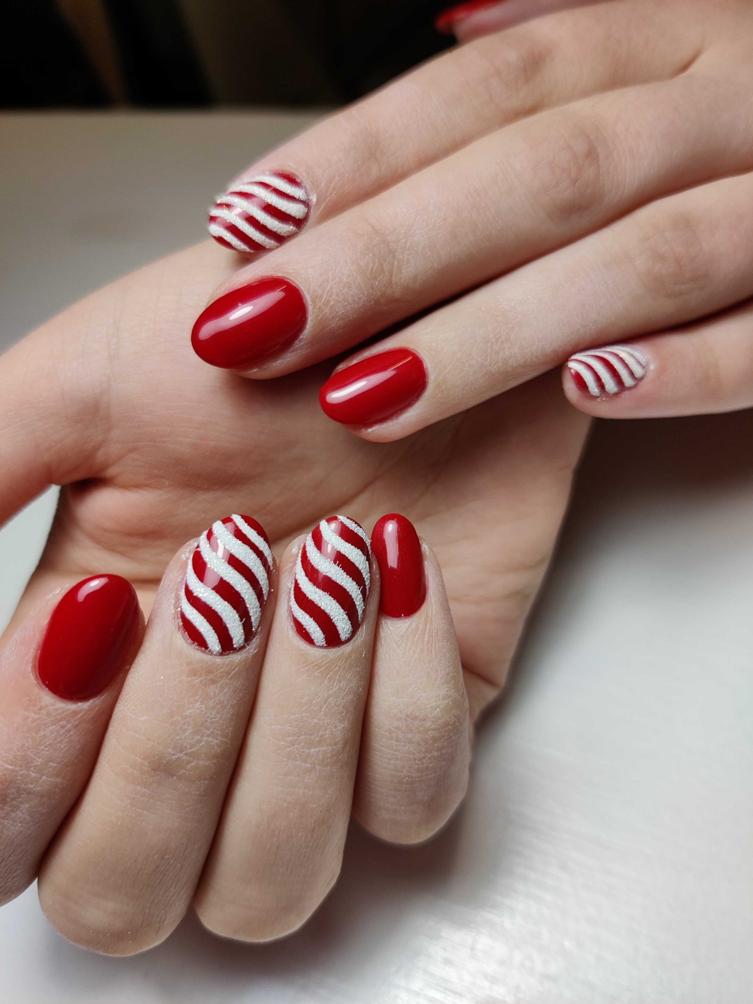 Glossy red oval nails with red and white candy cane striped accent nails