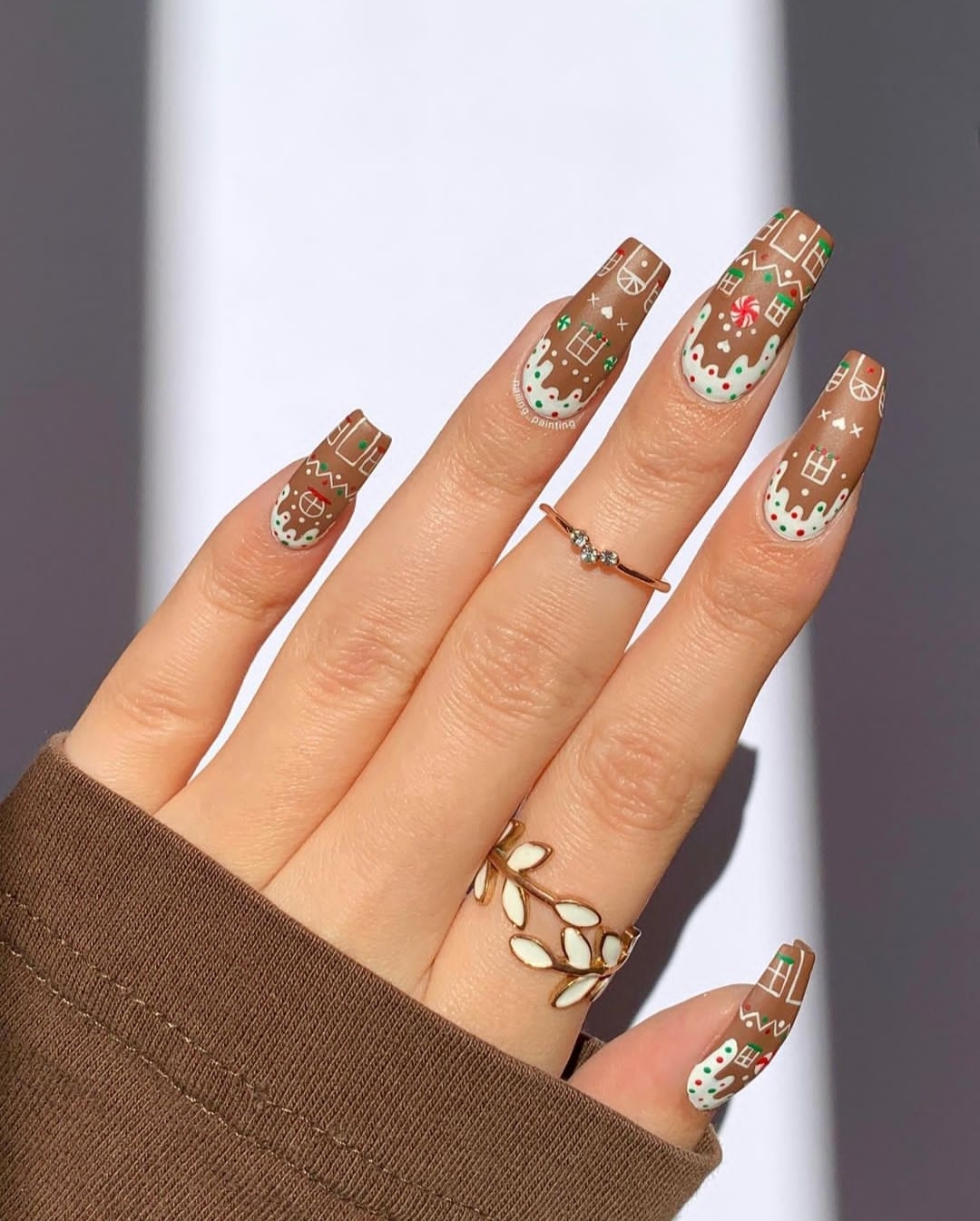 Gingerbread-brown nails decorated with white icing-style gingerbread-house art and sprinkles