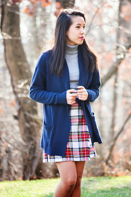 Woman wearing a navy cardigan and grey turtleneck with a red plaid mini skirt