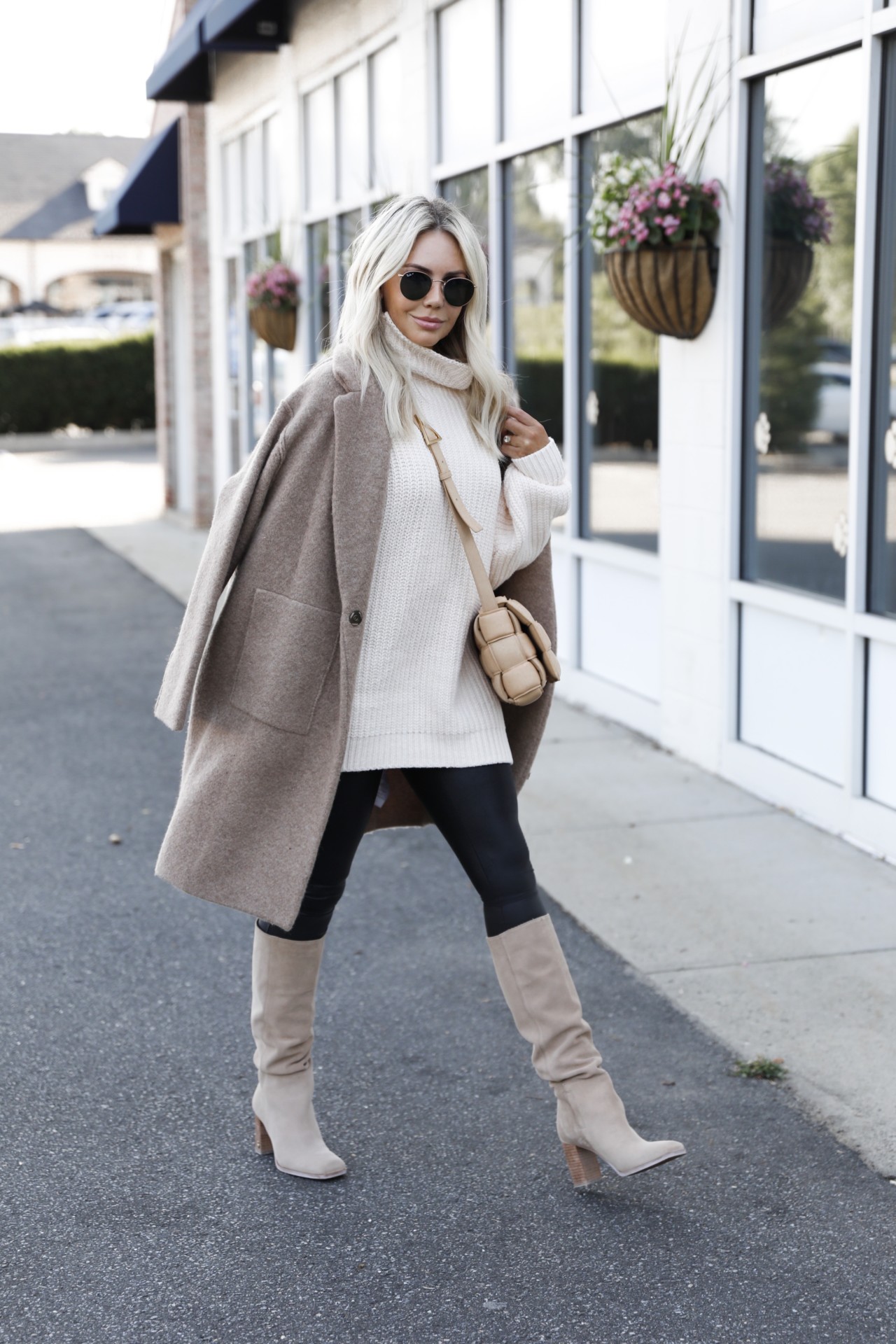 Woman in an oversized white turtleneck with black leggings, beige knee boots and a taupe coat
