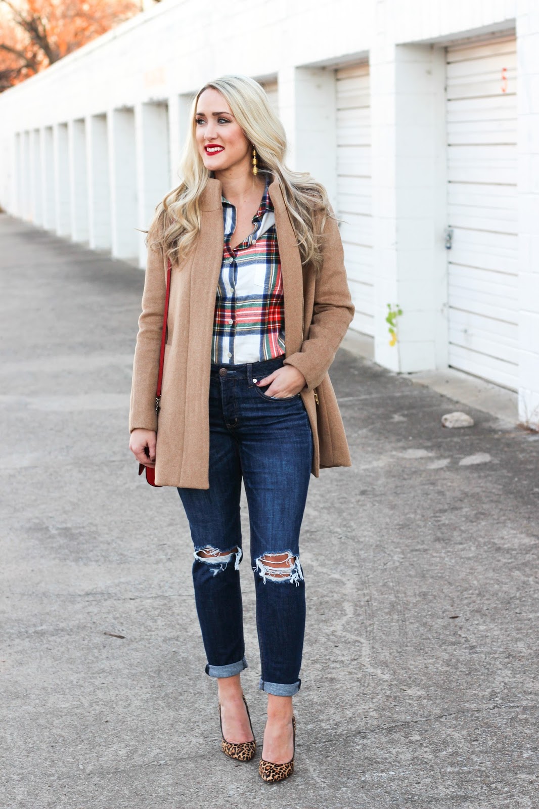 Woman in a camel coat over a plaid flannel shirt with ripped jeans and leopard heels