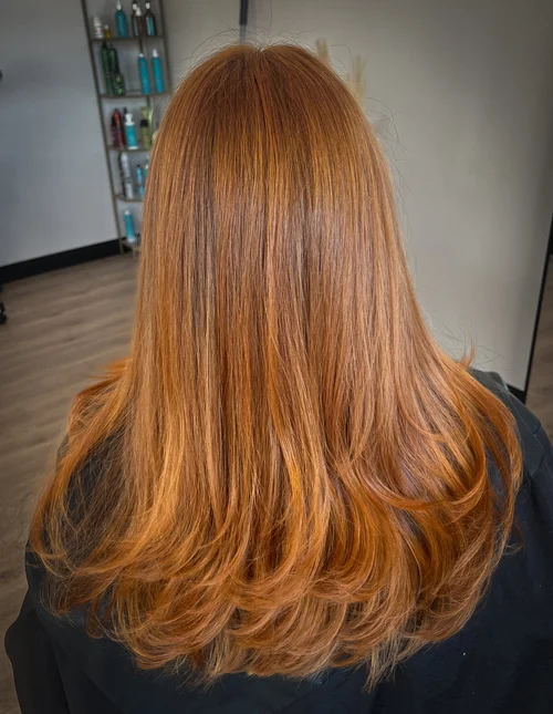 Long layered golden copper hair from behind in a salon