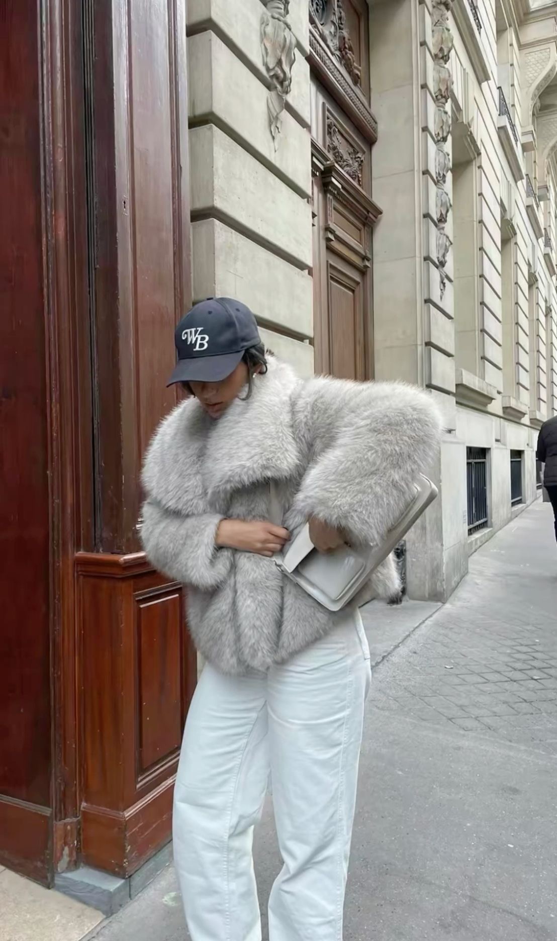 Woman in heather grey faux fur coat with white jeans and baseball cap