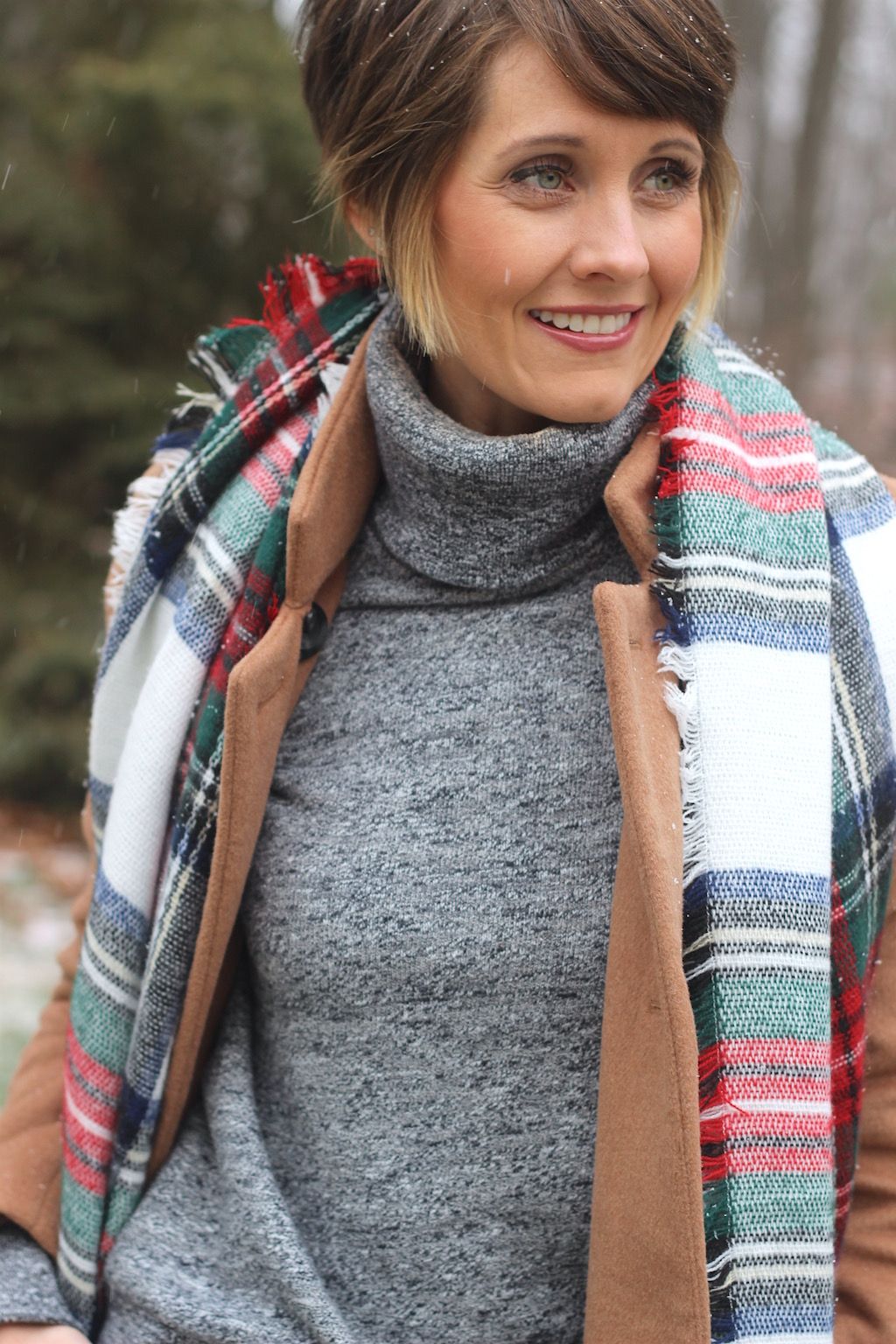 Close-up of a woman wearing a red and green plaid blanket scarf with a grey turtleneck and camel coat