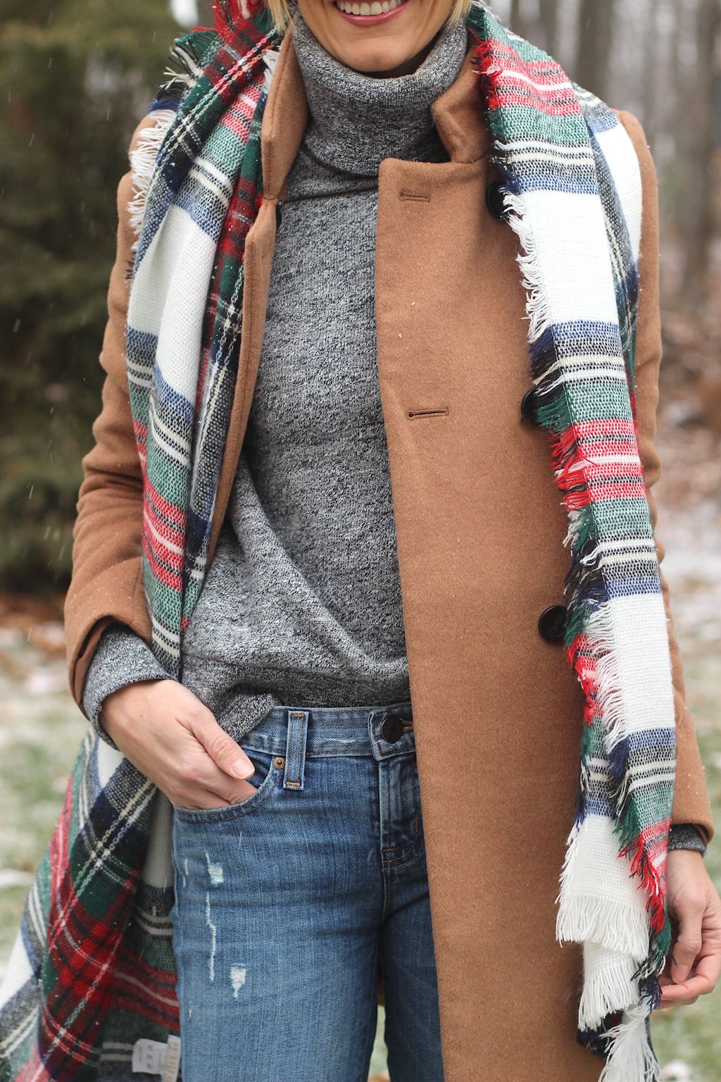 Woman wrapped in a blanket plaid scarf with a camel coat, winter street look