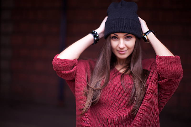 Woman wearing an oversized burgundy knit sweater with a black beanie