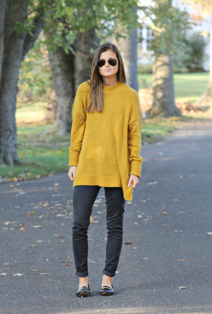 Woman wearing an oversized mustard tunic sweater with black skinny jeans and flats