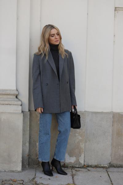Woman in a charcoal oversized blazer, black turtleneck, blue straight jeans, black heeled ankle boots and a black handbag
