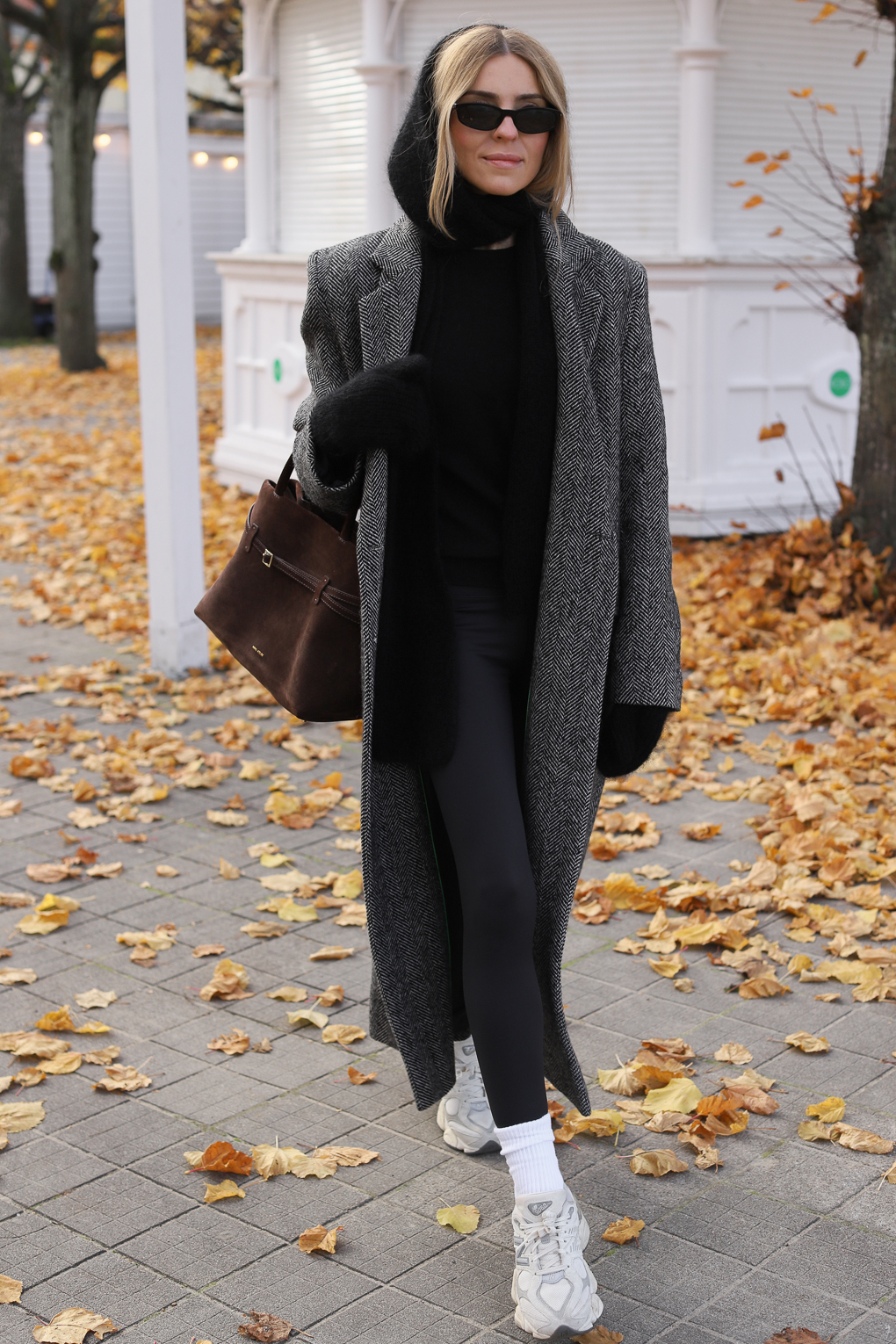 Woman in an oversized grey herringbone coat, black leggings and white sneakers with brown suede bag